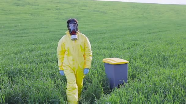 Uma mulher em um terno protetor amarelo fica no meio de um campo verde em uma máscara protetora de gás e mostra um gesto para chamar para parar e salvar o planeta - Filmagem, Vídeo