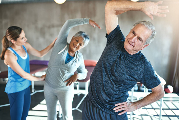 Rozciąganie, wsparcie i seniorów w fizjoterapii dla pomocy z fitness mięśni i wellness przez fizjoterapeutę. Ćwiczenia, trening i regeneracja stawów biodrowych i kręgosłupa dojrzałych klientów w klasie. - Zdjęcie, obraz