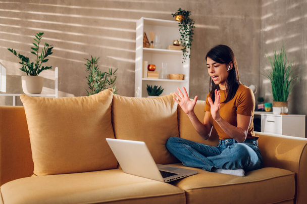 Hymyilevä valkoihoinen nainen käyttää kannettavaa tietokonetta istuessaan sohvalla kotona. Onnellinen nainen, jolla on videopuhelu tai online-tapaaminen asiakkaan tai työtovereiden kanssa. Kopioi tila. - Valokuva, kuva