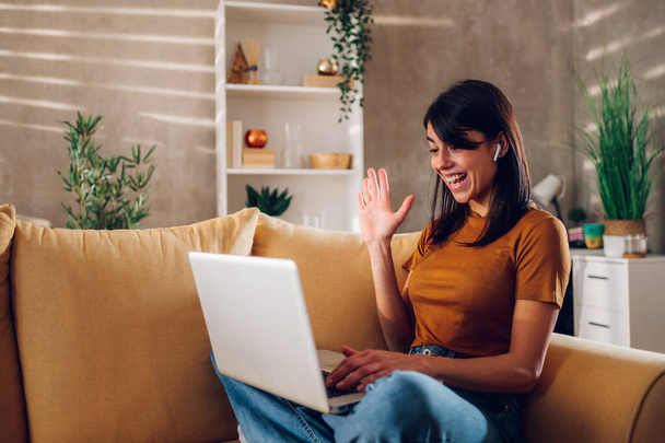 Porträt einer Frau mit Laptop und einem Online-Meeting, während sie von zu Hause aus arbeitet und zu Hause auf dem Sofa sitzt. Ein Videoanruf mit einem Kunden oder Kollegen, während Sie von zu Hause aus arbeiten. - Foto, Bild