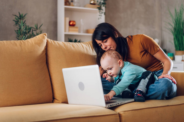 Mother sitting with son on couch and looking at a laptop. Happy caring single mom or nanny and little boy child watching cartoons or online shopping for kids toys. Children and technology. - Photo, Image