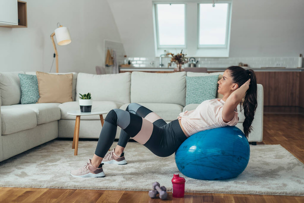 Mulher treinando em casa enquanto faz crunches na bola de fitness - Foto, Imagem