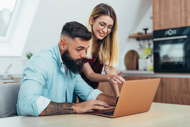 Girato di una giovane coppia felice utilizzando un computer portatile mentre si rilassa insieme a casa - Foto, immagini
