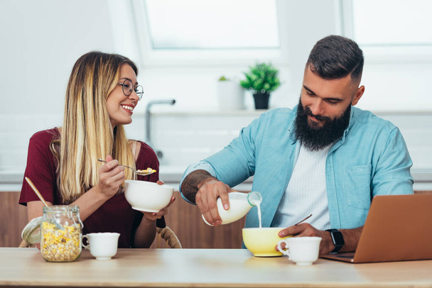Opname van een lachend jong echtpaar genietend van het ontbijt in de keuken - Foto, afbeelding