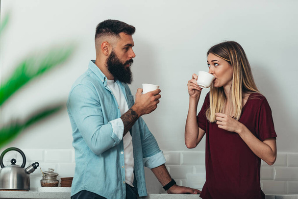 Young beautiful couple drinking coffee in the kitchen at home - Photo, Image