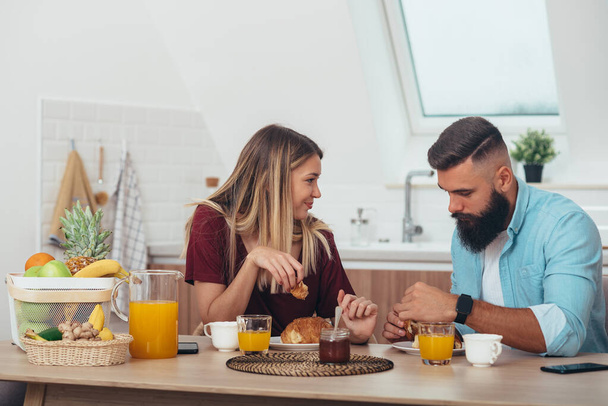 Gelukkig jong stel met een romantisch moment tijdens het ontbijt in de keuken thuis tijdens het drinken van sinaasappelsap - Foto, afbeelding