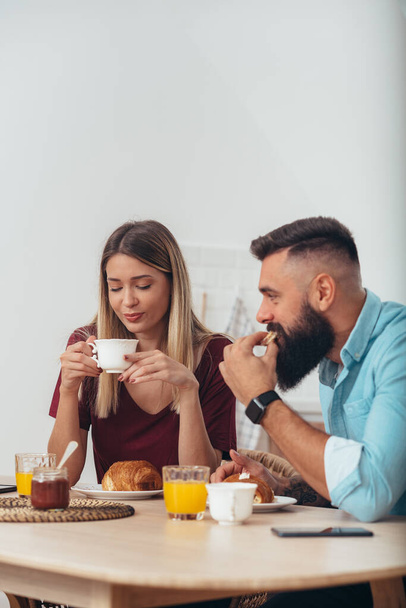Young couple drinking coffee during their breakfast in the kitchen at home - Photo, Image