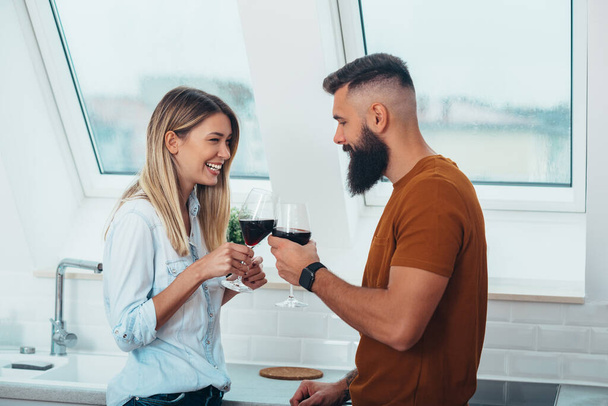 Съемка молодой пары, пьющей вино, стоя на кухне - Фото, изображение