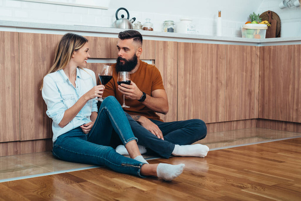 キッチンの床に座っている間、愛情のあるカップルの飲酒ワインのショット - 写真・画像