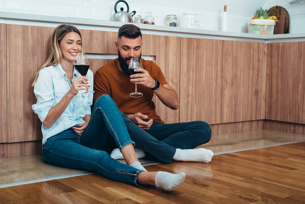 Foto de una pareja joven y cariñosa bebiendo vino en la cocina - Foto, imagen