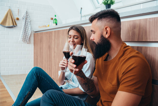 Aufnahme eines jungen Paares, das zu Hause in der Küche ein Glas Wein trinkt - Foto, Bild
