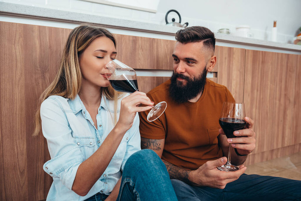 Mutfakta şarap içerken birbirlerine eşlik eden mutlu genç bir çiftin fotoğrafı. - Fotoğraf, Görsel