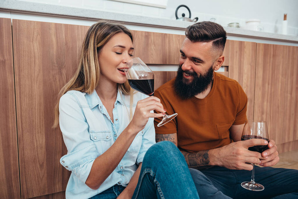 Μια φωτογραφία ενός νεαρού ζευγαριού που απολαμβάνει ένα ποτήρι κρασί στο σπίτι. - Φωτογραφία, εικόνα