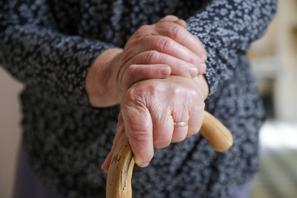 Chodící postižení. Detailní záběr starší postižené ženy opírající se o vycházkovou hůl. Stará žena ruce drží rukojeť hole. - Fotografie, Obrázek