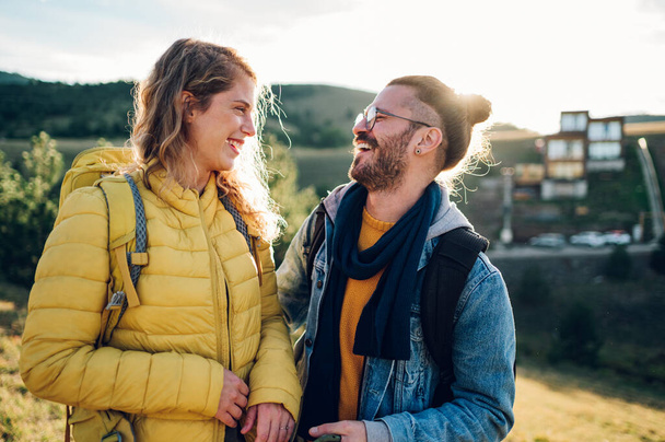 Portrait of a beautiful woman and man travelers enjoying hike and nature view during rest in the fresh air. Smiling and looking at each other. Couple walking on a mountain path during their vacation. - Photo, Image