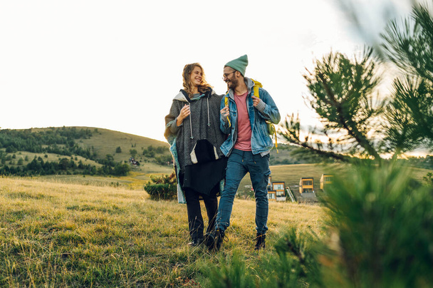 Portret pary wędrowców spacerujących górskim trawiastym szlakiem i spędzających wspólnie czas na łonie natury. Portret mężczyzny i kobiety przechodzących górską ścieżką. Romantyczny wypad. - Zdjęcie, obraz