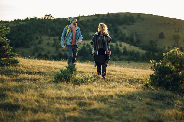 Portrait of a traveling couple in hiking gear walking in the mountains at sunset and having fun. Smiling spouses walking together down a hillock and enjoying the nature during a sunset.Copy space. - Photo, Image