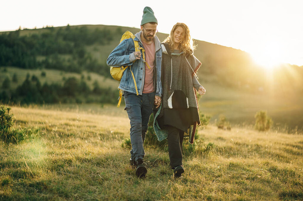 若い旅行者のカップルは日没の間に暖かい晴れた夜に美しい山のトレイルを歩いている間手を握ります. 田舎での休暇で幸せな若者と女性. コピースペース. - 写真・画像