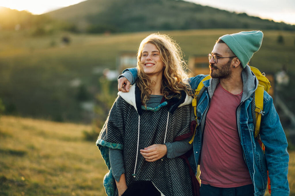 Close shot of a caucasian couple hiking in mountains with backpacks and enjoying their adventure on a vacation. Active fit lifestyle. Man hugging woman and looking at her while she is smiling. - Photo, Image