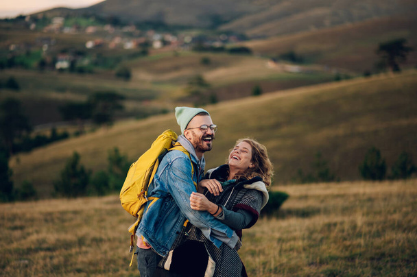 Un paio di escursionisti che si abbracciano e sorridono camminando lungo un sentiero erboso di montagna e trascorrendo il loro tempo insieme nella natura. Ritratto di uomo e donna che si divertono trascorrendo del tempo in montagna - Foto, immagini