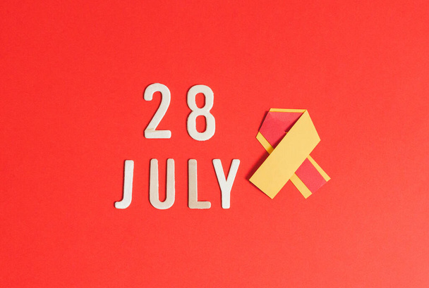 Egy sárga-piros papír szalag fa számok és betűk Július 28-án fekszik a közepén egy piros háttér, lapos feküdt közelkép. - Fotó, kép