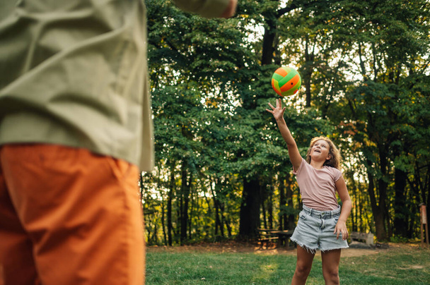An active girl is playing volleyball in nature with her father. A playful daughter is hitting a ball while playing sports in nature with her parent. A sporty family playing volleyball on meadow. - Photo, Image
