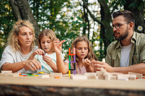 Сім'я проводить день у природі, граючи з освітніми іграшками на пікніку. Сім'я сидить за столом у природі і складає вежу з різнокольорової дерев'яної плитки. Веселий час, освітні ігри, командна робота. - Фото, зображення
