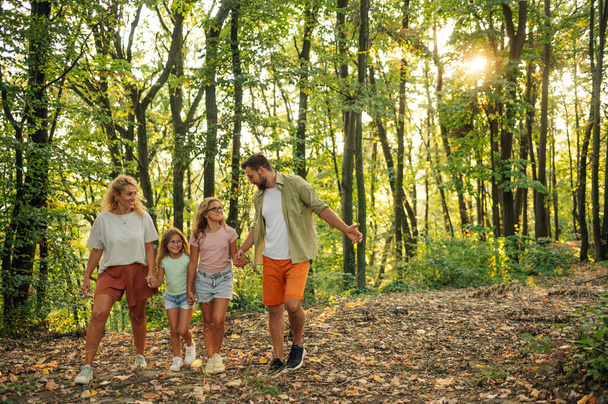 Padres alegres tomados de la mano con las hijas y dando un paseo por la naturaleza. La familia feliz está teniendo una aventura mientras explora las bellezas naturales y el bosque. La familia pasa el fin de semana en la naturaleza. - Foto, Imagen