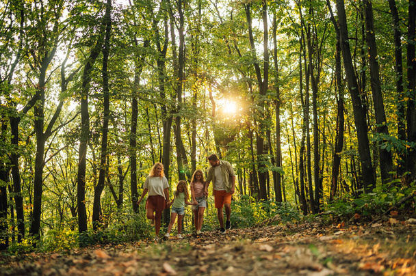 Egy boldog család teljes hossza fogja egymás kezét és felfedezi az erdőt. Szülők és lányok fogják egymás kezét és túráznak az erdőben, miközben napos nyári napot töltenek az erdőben. Családi kalandozás a természetben. - Fotó, kép