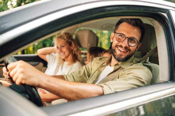 Portret przystojnego uśmiechniętego mężczyzny prowadzącego samochód. Ojciec korzystających z podróży w weekend i podróży samochodem z rodziną. Pojęcie urlopu i podróży. - Zdjęcie, obraz