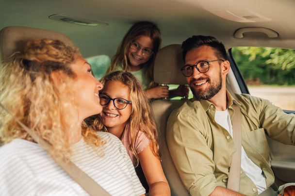 Portret szczęśliwej białej rodziny jeżdżącej nowym samochodem lub mającej jazdę próbną w mieście. Rodzice i córki spędzają wakacje podróżując samochodem i ciesząc się podróżą. Przestrzeń kopiowania. - Zdjęcie, obraz