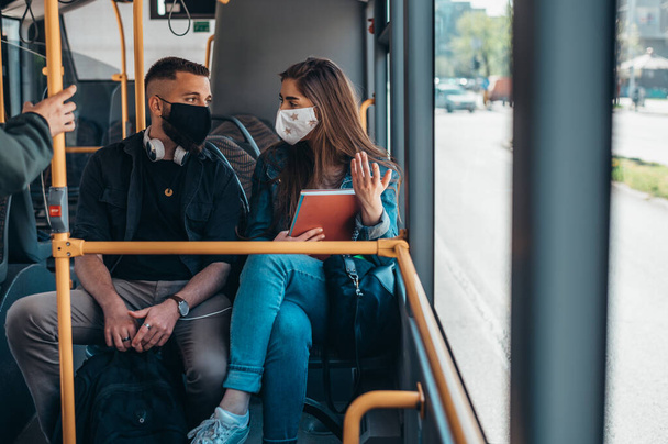 Young couple wearing protective masks riding a bus and talking to each other - Фото, изображение