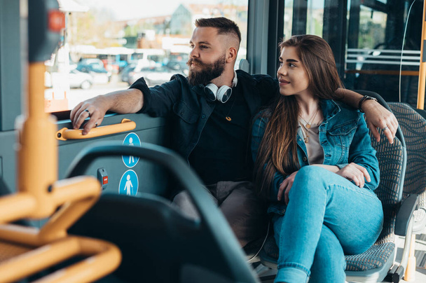 Giovane coppia romantica seduta in un autobus in movimento mentre abbraccia e guarda fuori attraverso la finestra - Foto, immagini