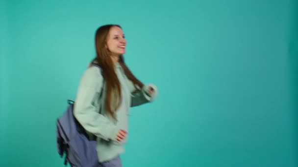 Joyous girl holding rucksack looking around, inviting others to join her, doing hand gesturing. Jolly teenager doing inspecting gesture, discovering new place, isolated over studio backdrop, camera B - Footage, Video