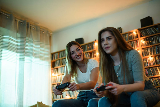 Kaksi parasta ystävää pelaa videopelejä rentoutuessaan kotona sohvalla - Valokuva, kuva