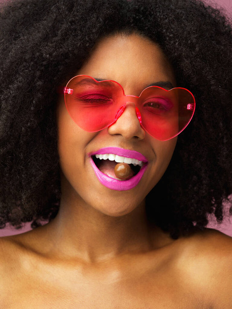 Portrait, chocolate and girl with glasses, fashion and shades with sweet treat, candy and confidence. Face, person and woman with funky eyewear, heart shape and cocoa with style, winking and snack. - Photo, Image