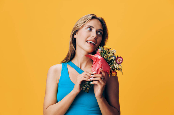 Сияющая женщина, держа яркий букет цветов на веселом желтом фоне, уверенно глядя в камеру - Фото, изображение