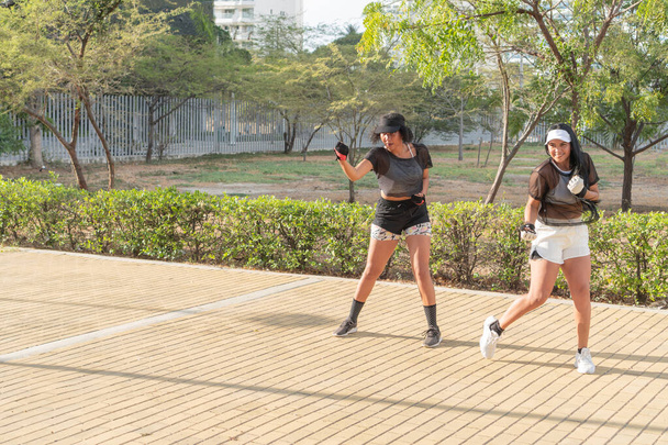 Two women in athletic wear exercising together in an urban park, engaging in a dynamic outdoor workout on a sunny day. - Photo, Image