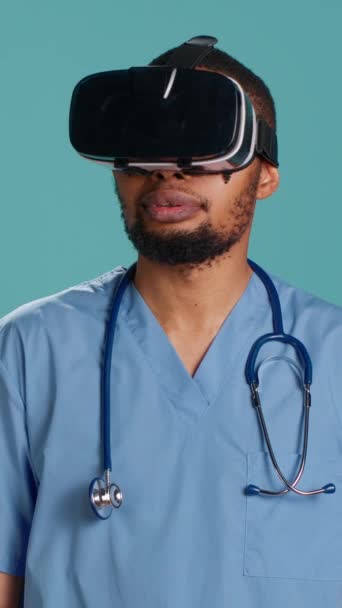 Вертикальне відео афроамериканського лікаря, який носить окуляри віртуальної реальності, дистанційно працюючий пацієнт. Член лікарні з використанням високотехнологічного медичного пристрою vr, ізольований на фоні студії, камера А - Кадри, відео