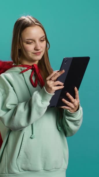 Verticale video Jong meisje draagt superheld kostuum voor Halloween browsen social media feed op tablet, studio achtergrond. Vrouw verkleed als stripboek held met plezier lezen berichten op het apparaat - Video