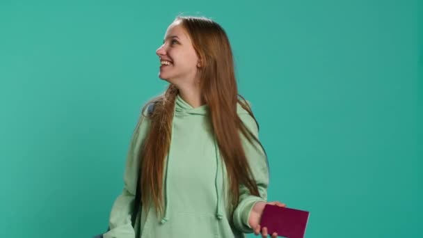 Joyous young traveler holding passport, going on vacation, looking around after arriving in new place. Happy girl travelling, sightseeing, visiting attractions, studio background, camera A - Footage, Video