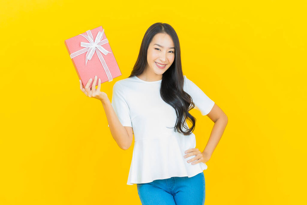 Portré gyönyörű fiatal ázsiai nő mosoly piros ajándék doboz sárga színű háttér - Fotó, kép
