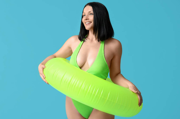 Красива молода жінка в стильному зеленому купальнику з надувним кільцем на синьому фоні - Фото, зображення