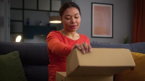 Happy usměvavá těhotná Afroameričanka dívka žena matka těší těhotenství doma gauč rozbalit box balíček vybalení objednávky dodání obchod oblečení nákupní připravuje k porodu - Záběry, video