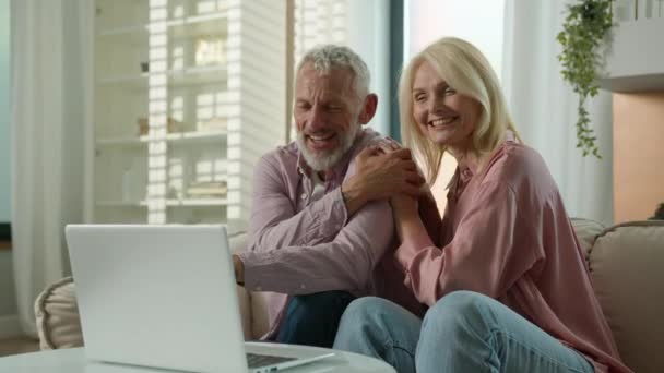 Onnellinen vanhempi perhe Valkoihoinen pari iäkäs nainen mies puhuu verkossa videopuhelu nainen mies käyttää kannettavaa tietokonetta pc kypsä aviomies vaimo nauraa halata puhua internet virtuaalinen chat sisätiloissa olohuone - Materiaali, video