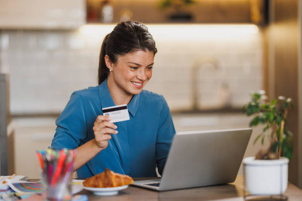 Unternehmerin arbeitet am Laptop und bezahlt Rechnungen mit Kreditkarte, während sie von zu Hause aus arbeitet. - Foto, Bild