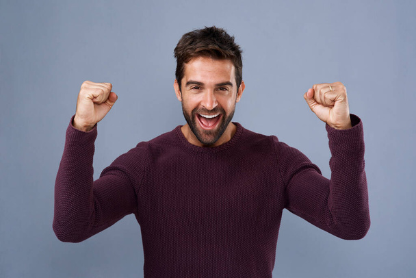Celebration, cheering and man in studio, happy and portrait of success, smile and wow for news of sale. Blue background, mockup and fist of person, win and lucky in lottery, giveaway or reward in USA. - Photo, Image