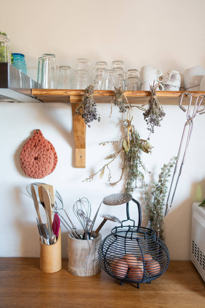 Detalle rústico de la cocina, cuenco con cucharas y cucharones, estante con vasos y tazas. Colgar hierbas aromáticas y huevos en un recipiente. - Foto, Imagen