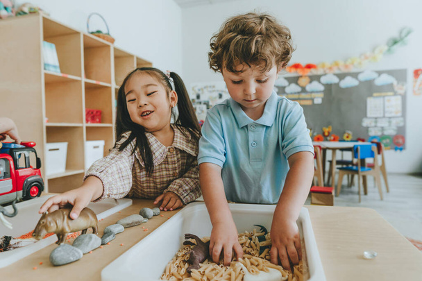 Kinderen spelen en ontwikkelen tactiliteit met speelgoed dierlijke figuren in bulk granen en pasta op de kleuterschool - Foto, afbeelding