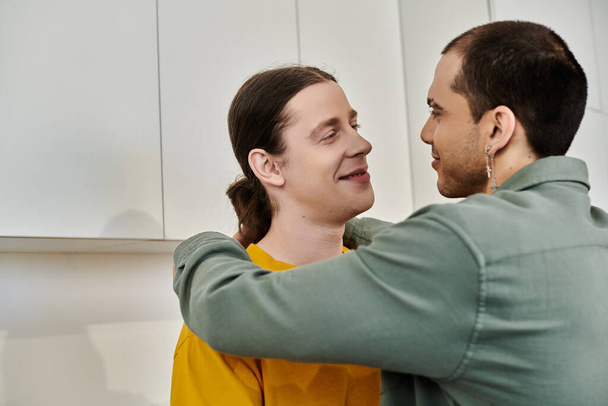 Um jovem casal gay se abraça em um apartamento moderno, compartilhando um momento terno de carinho. - Foto, Imagem